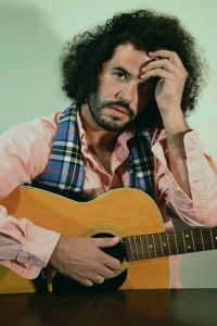 daniel-bejar-destroyer-in-pink-shirt-and-plaid-scarf-holding-guitar-against-green-background-googleganger-2 Daniel Bejar Destroyer in pink shirt and plaid scarf holding guitar against green background