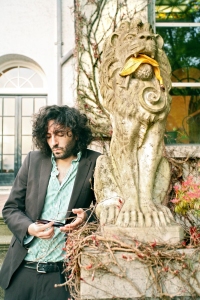 Daniel Bejar Destroyer holding sunglasses against a lion statue with a banana peel in it's mouth.